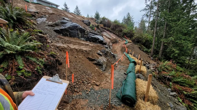 Steep hillside lot showing exposed rock and soil layers with engineering stakes on Vancouver Island